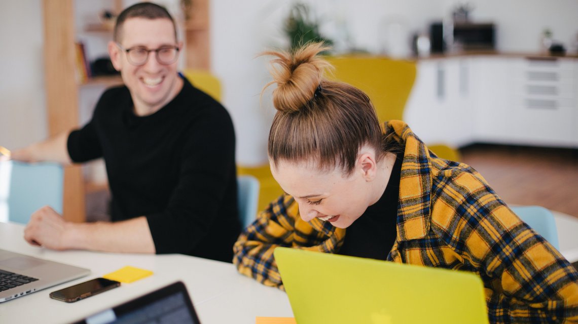 Bachelor Soziale Arbeit & Diakonie Eine Studentin und ein Student sitzen vor ihren Notebooks am Tisch und lachen.