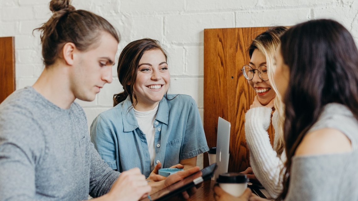 Drei Studentinnen und ein Student sitzen im Café und reden miteinander.