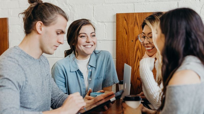 Drei Studentinnen und ein Student sitzen im Café und reden miteinander.