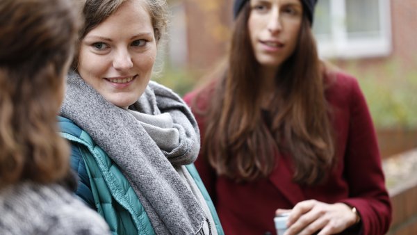 Drei junge Frauen stehen vor der Hochschule und unterhalten sich.