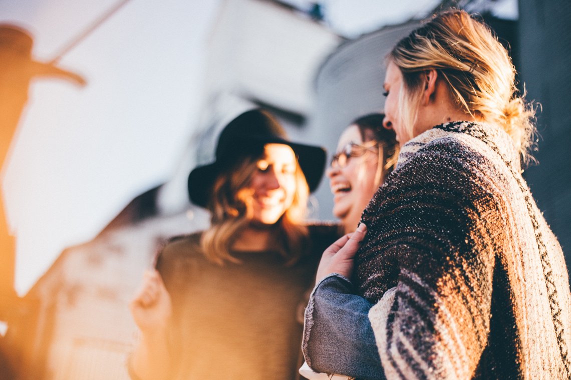 Drei junge Frauen, Studierende, im Sonnenlicht vor einem Gebäude.